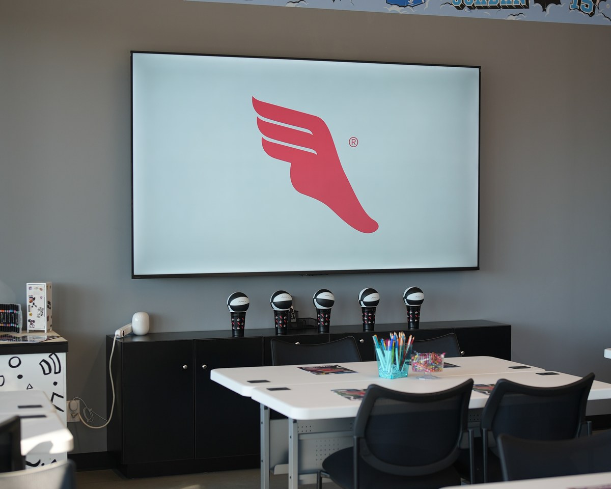 The community room set with tables and chairs facing the 100-inch TV screen